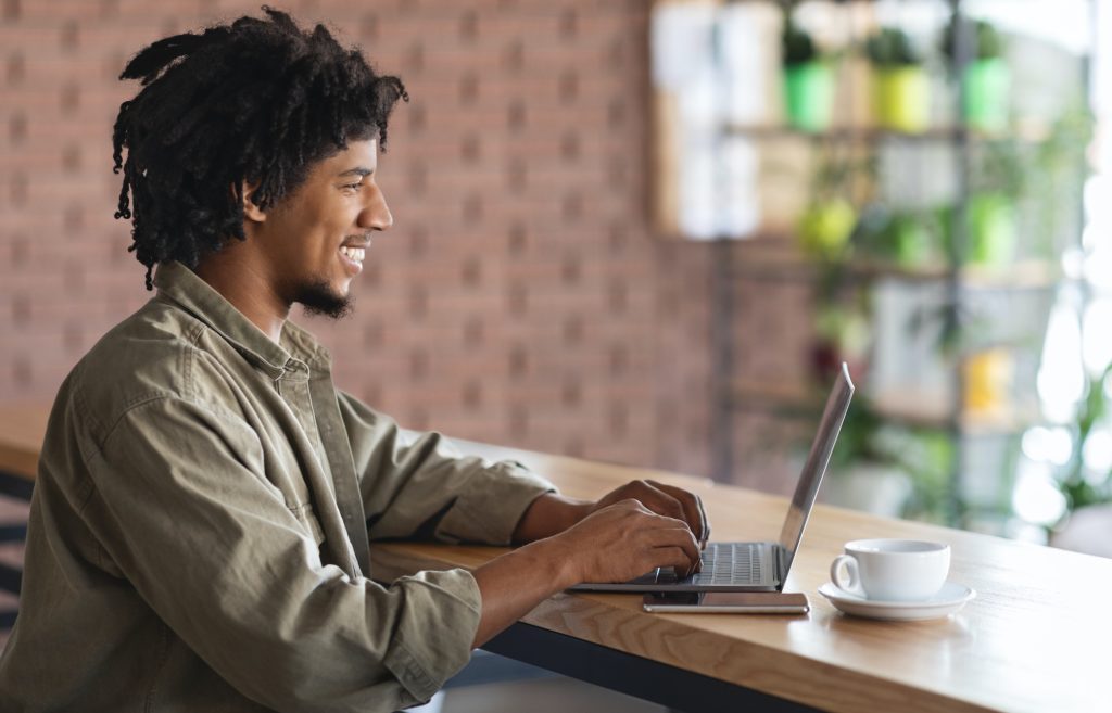 Remote Work. Young African American Freelancer Guy Working With Laptop At Cafe