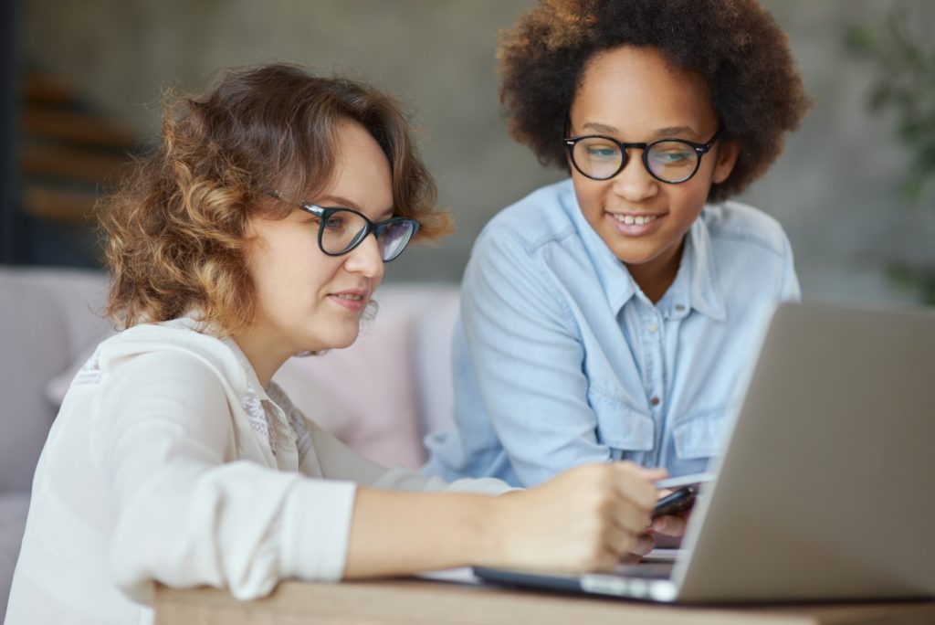 Portrait of attractive female teacher helping her little student, teen schoolgirl with homework